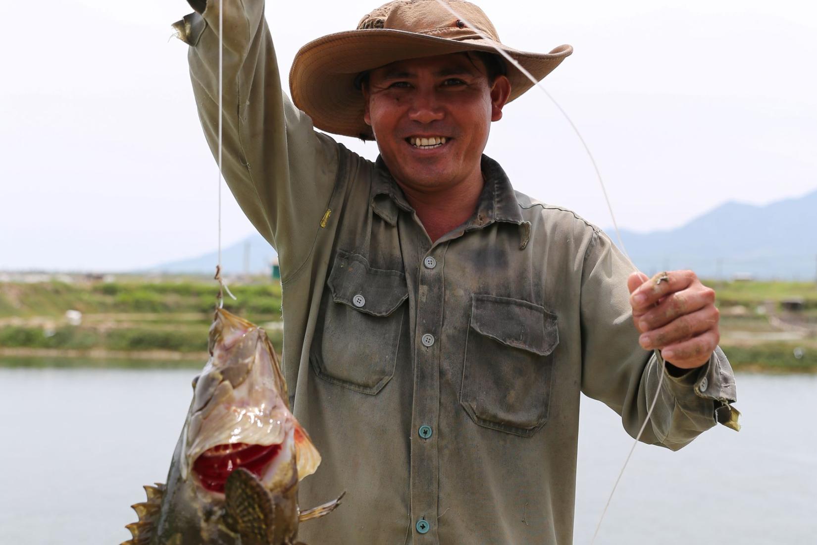 Man standing in boat smiling and holding up a large fish