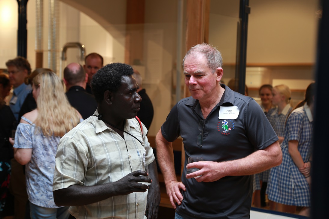 two men talking in a room full of people