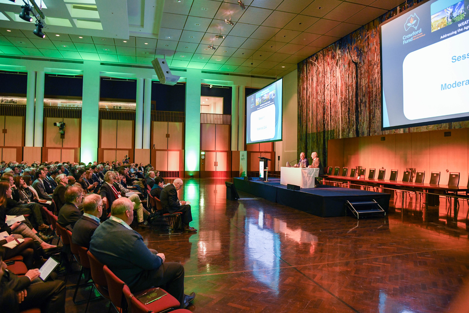 a large room full of people with 2 speakers at the front 