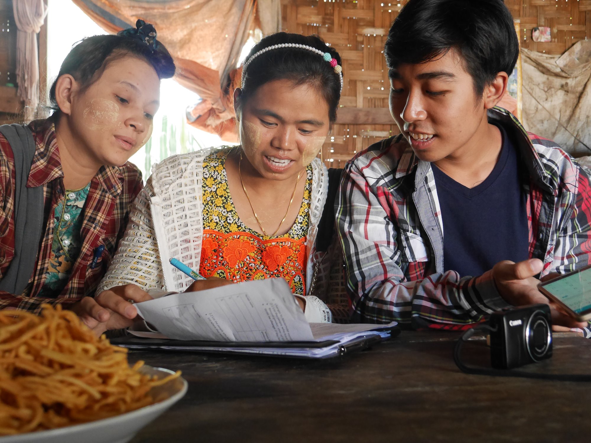 Three women in a hut filling out a paper form