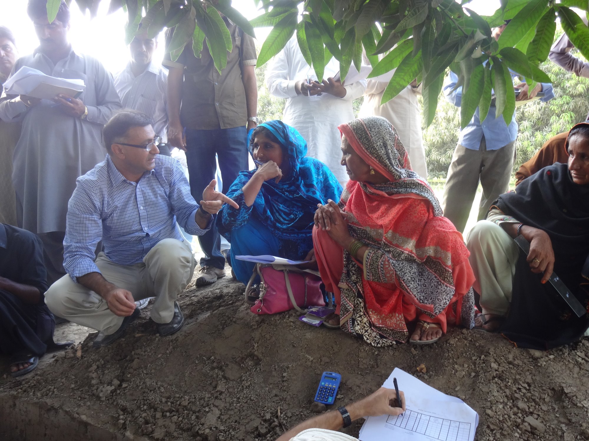 Group of people on mound of soil listening to a man speak