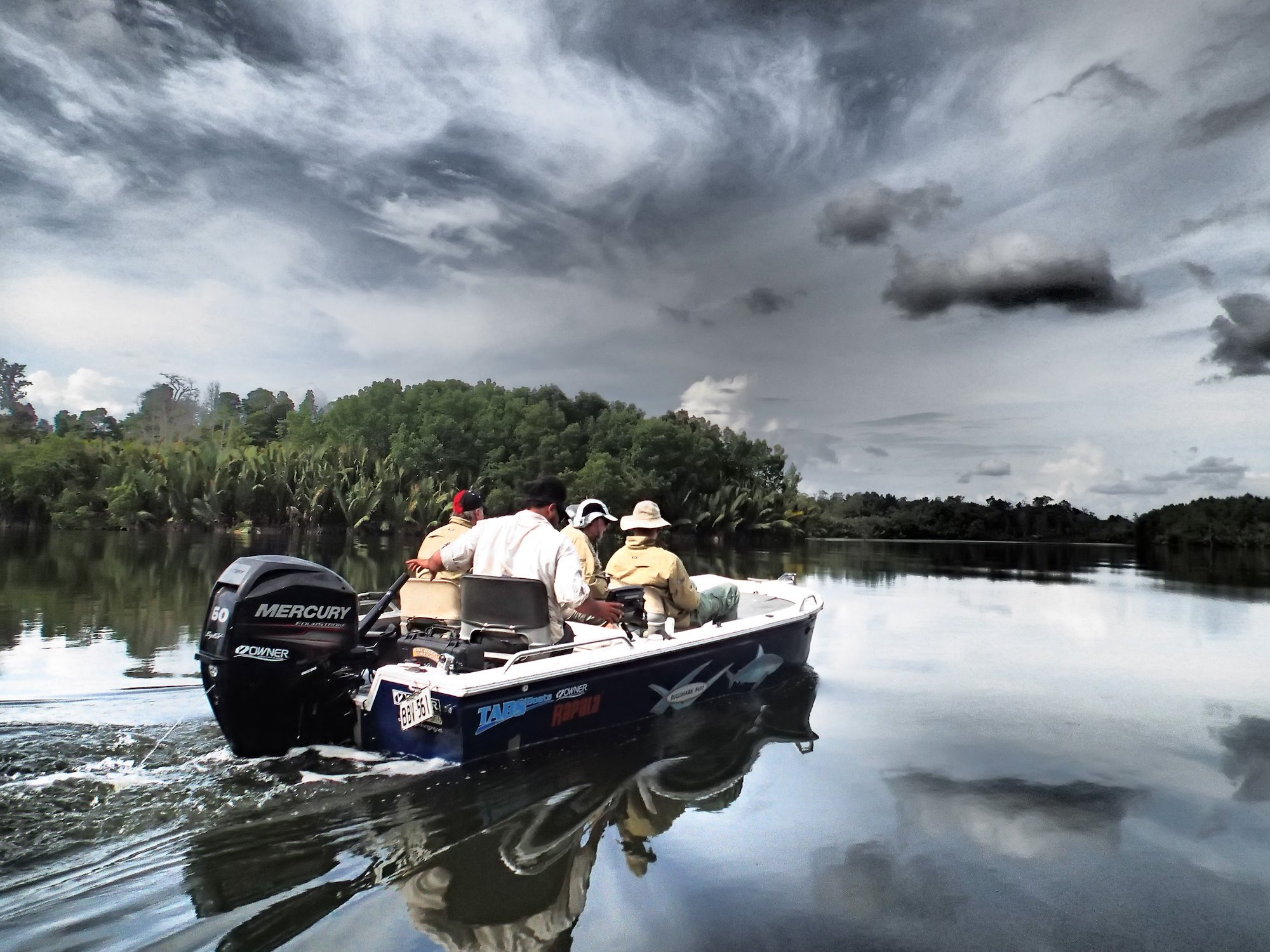 Four men in a speedboat on a river with storm clouds above