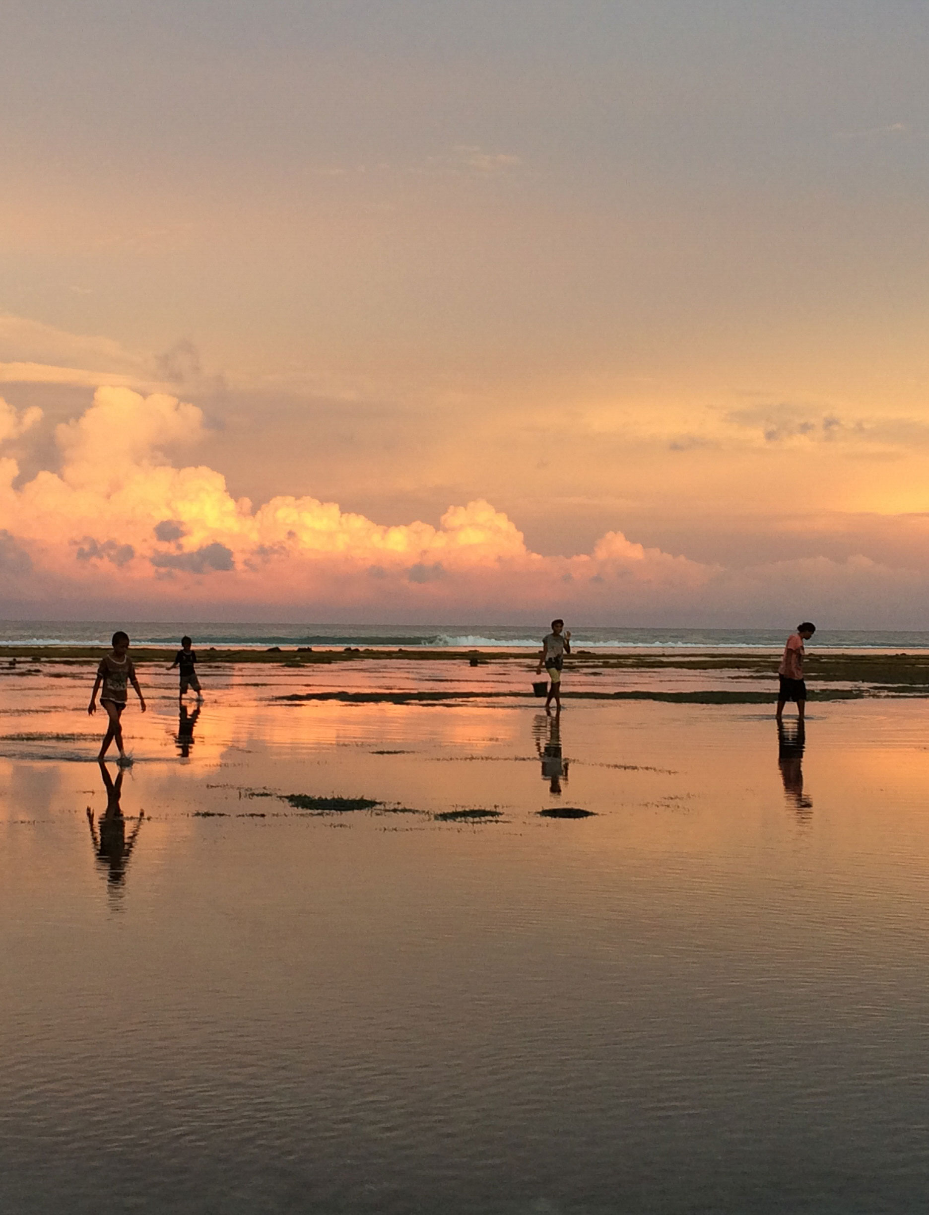 Children walking along a beach at sunset, holding buckets