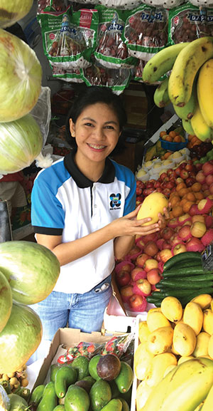A lady holds a mango in a fruit market stall