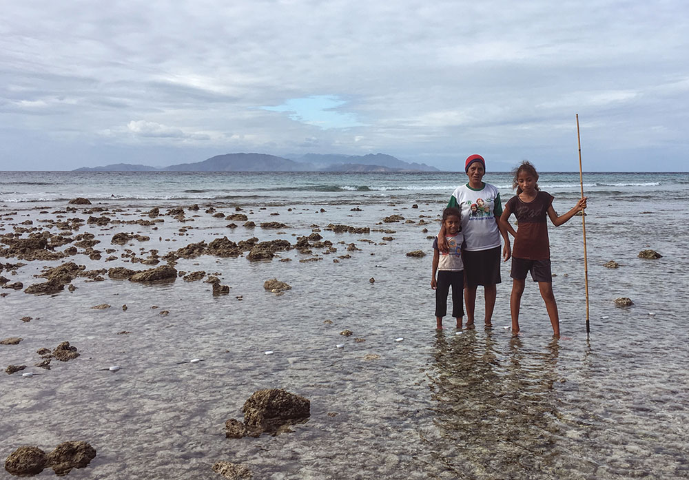 Three people standing in the shallows of the ocean with a fishing spear