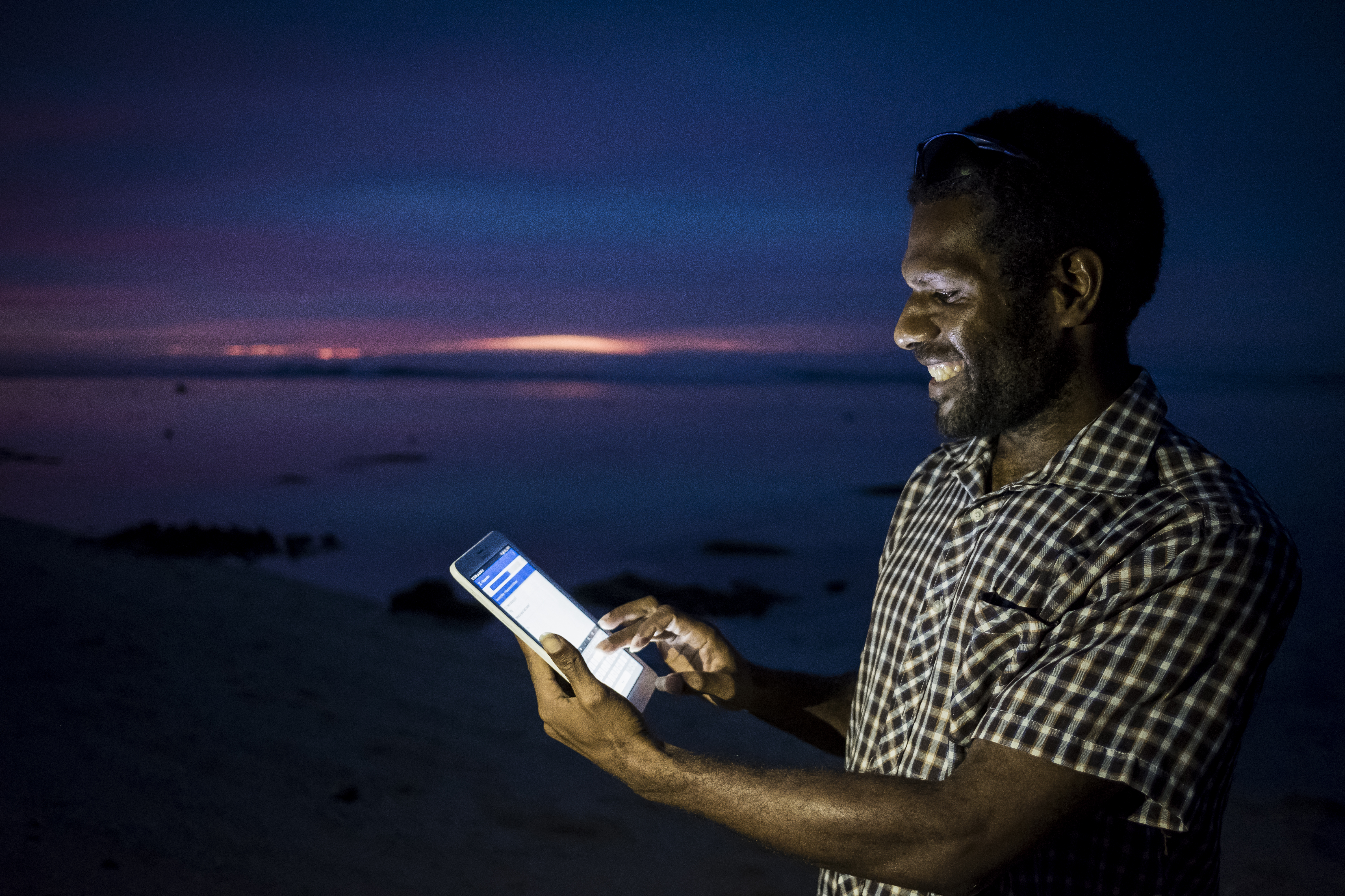 Man looking a mobile device in the evening time with ocean in the background