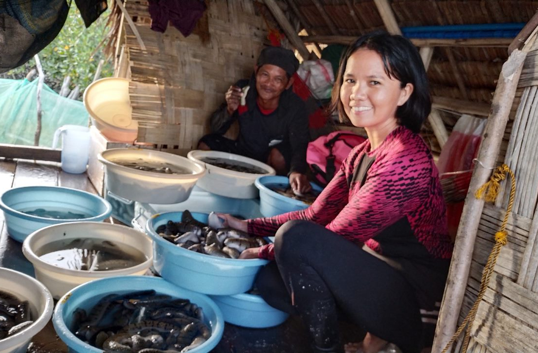 Woman and man sitting next to tubs of fish