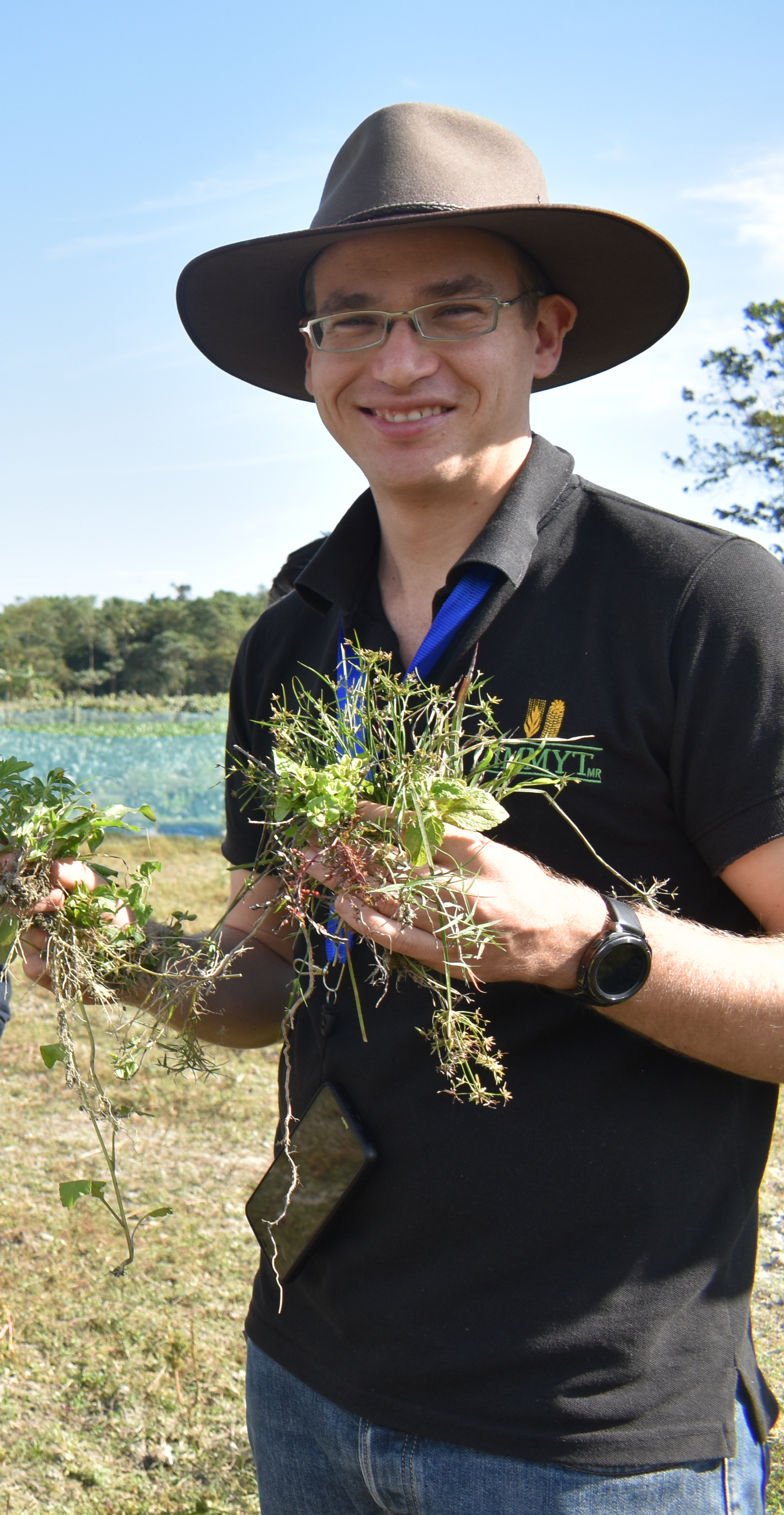 Person wearing hat stand outside holding handfuls of plants