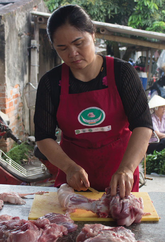 A person cuts pork on a chopping board in a Vietnamese wet market