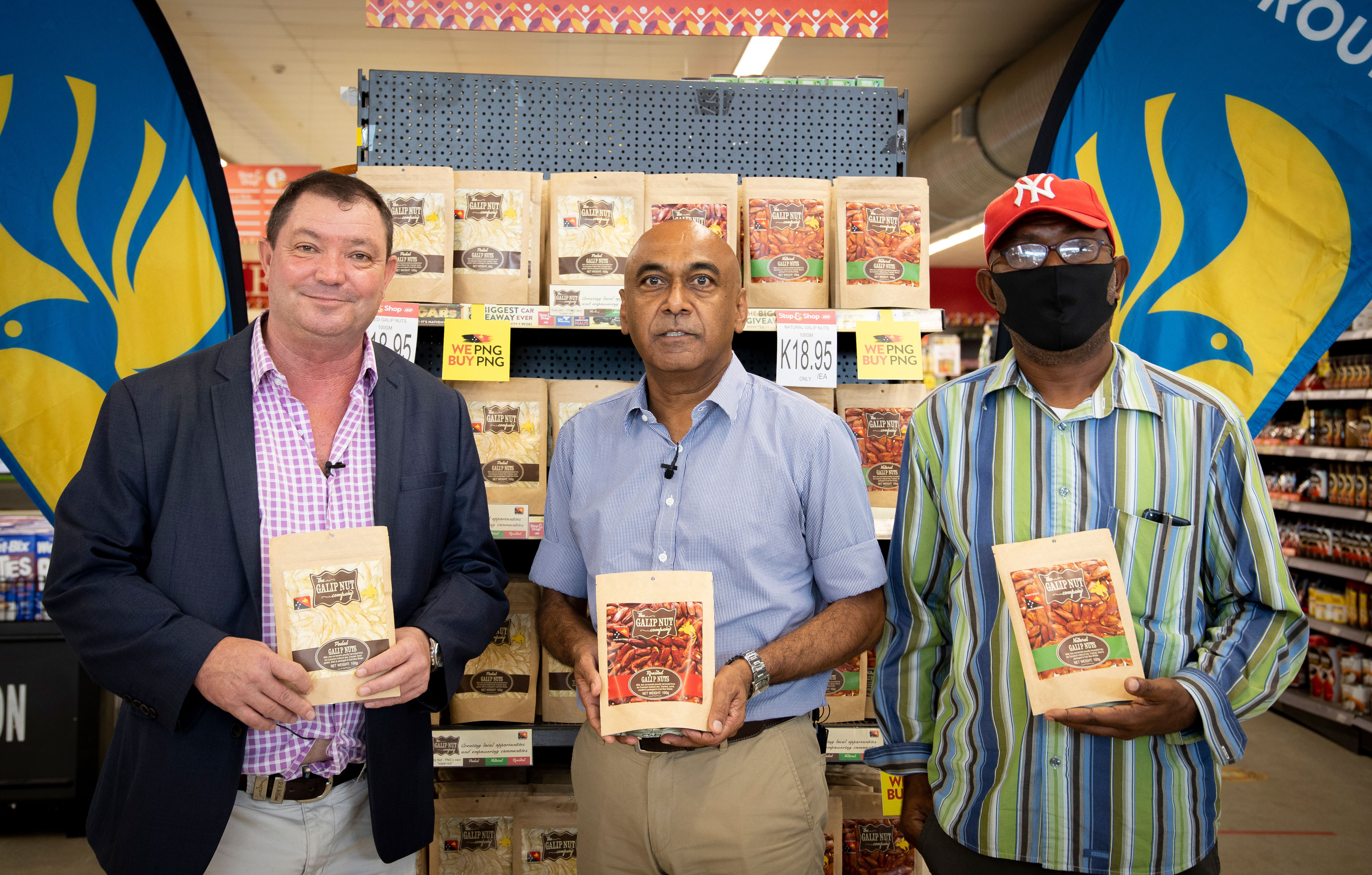 Three men holding bags of galip nuts in front of display stand