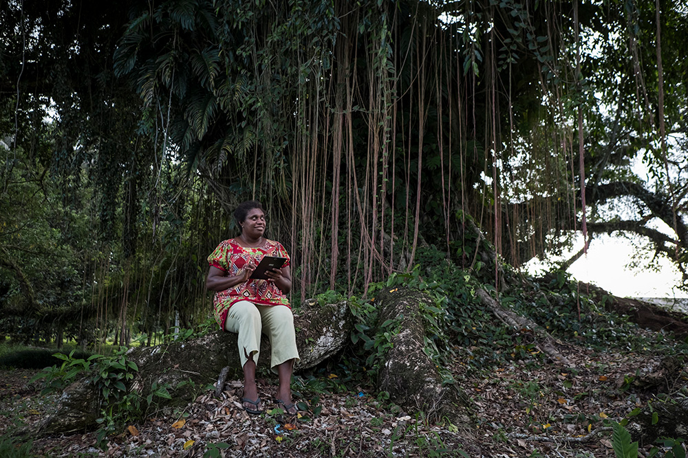 A woman sitting in a forest, with a smart tablet in her hands, looking into the distance.