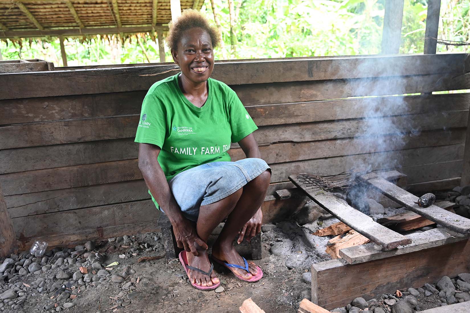 A woman sitting by a fire, smiling at the camera.