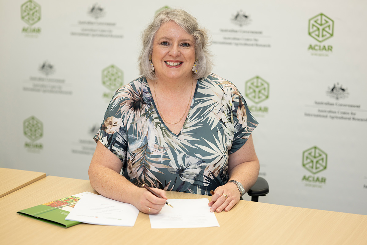 A woman sitting at a table with pen in hand, smiling at the camera