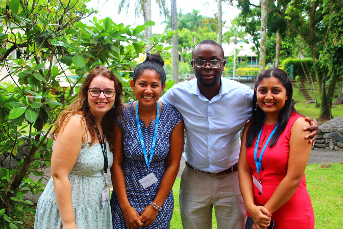 Three women and one man with arms around each other, smiling at the camera. 