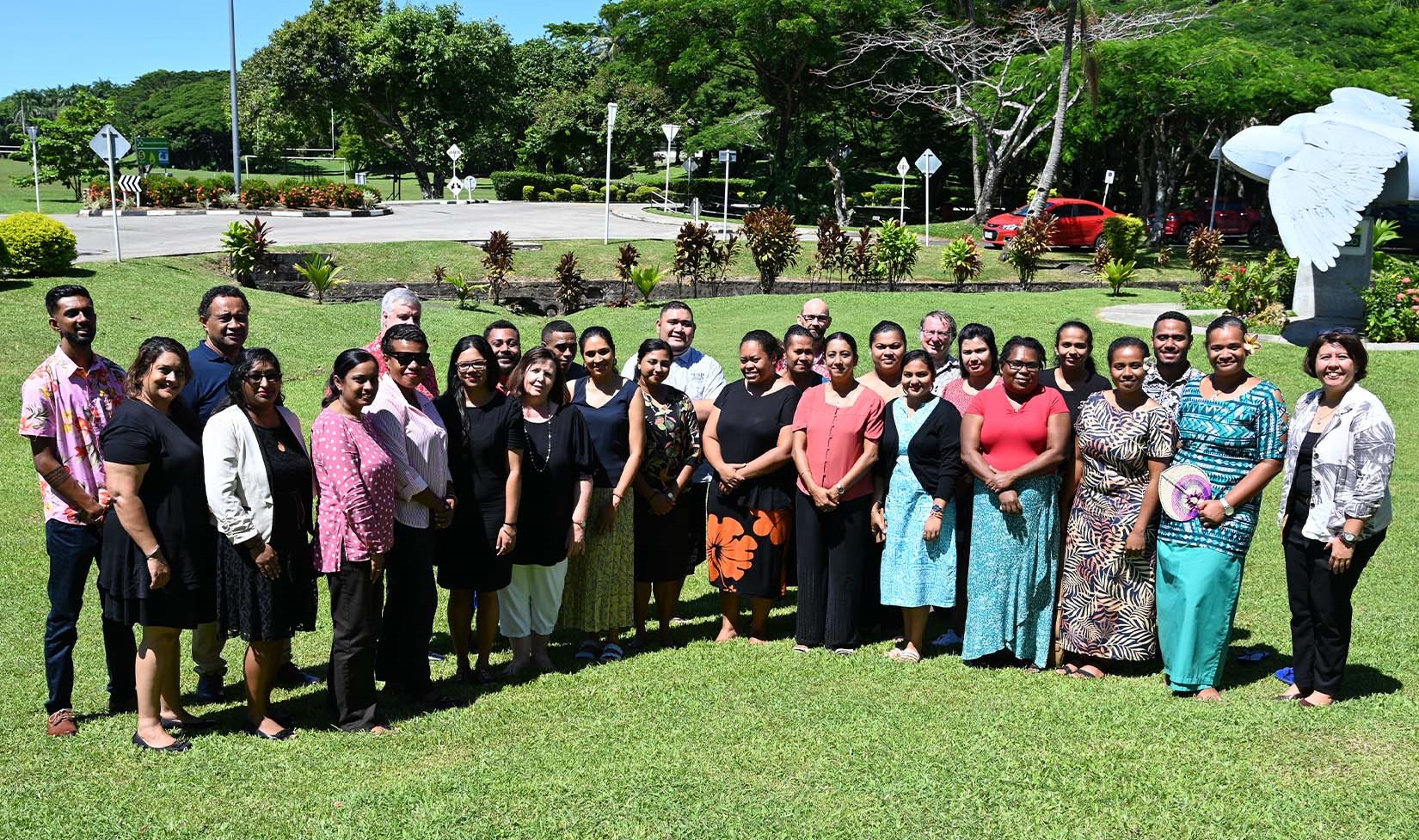 A large group of people standing together on a green lawn, smiling at the camera.