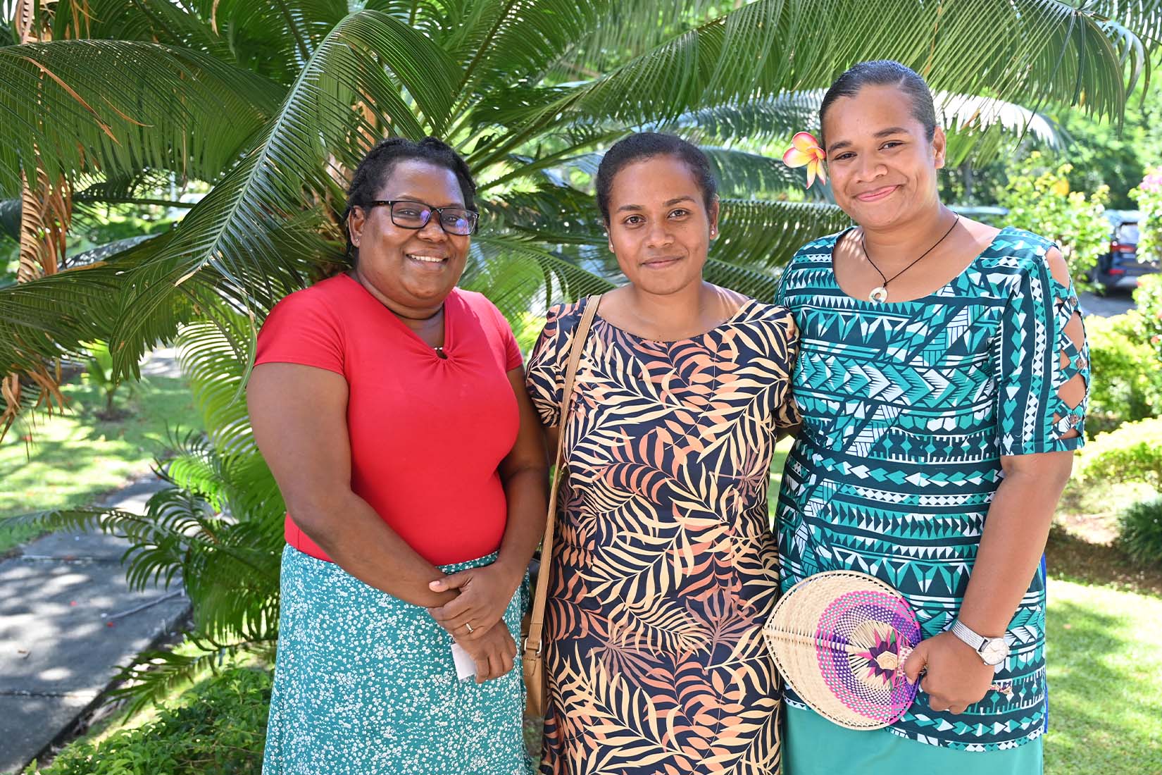 Three women standing in front of palm trees, smiling at the camera.