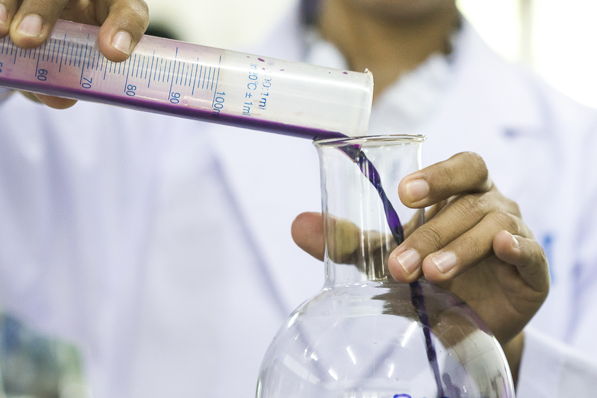 person in a lab coat, pouring liquid
