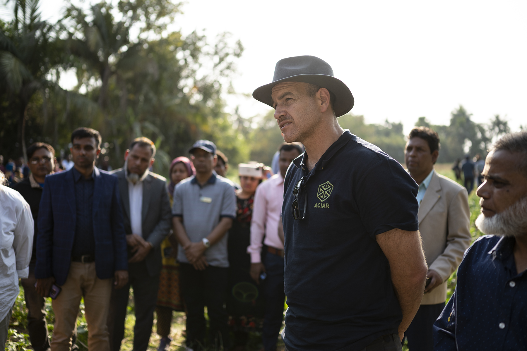 A group of people in a field, listening to a talk