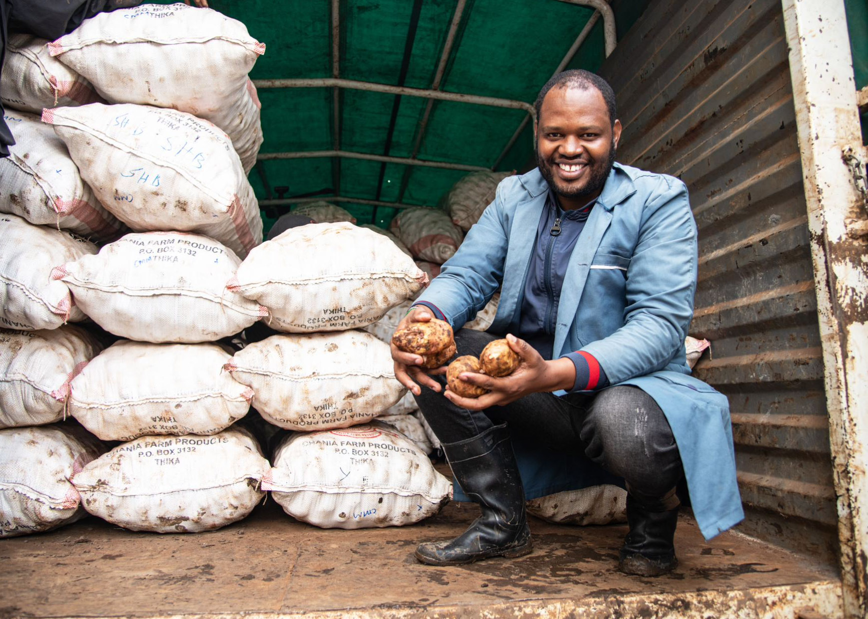 A potato farmer in a blue coat smiling with his produce
