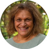 A head shot of Dr Audrey Aumua. She has shoulder-length curly hair and is wearing a light-colour top. She is smiling broadly. 