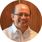 A head shot of Dr Reynaldo V Ebora. He is a balding man, wearing glasses and a white-collared shirt. 