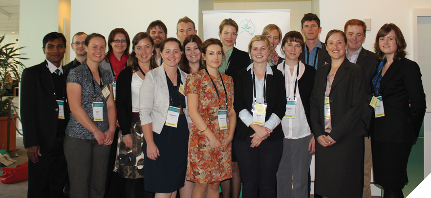 A group photo of men and women standing in a room. Many of them are wearing nametags. Their dressed semiformally, in suits, jackets, dresses and slacks. 