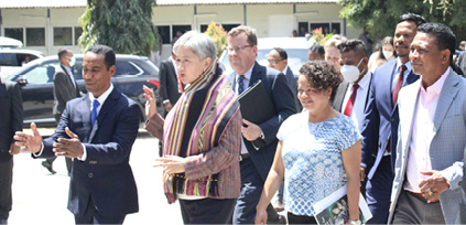 A group of men and women are standing in front of a building. The men are wearing suits and ties and the women dress clothes. Some people are clapping their hands. 