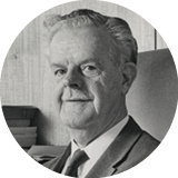 A black-and-white head shot of Sir John Crawford. He is wearing a suit and a tie.