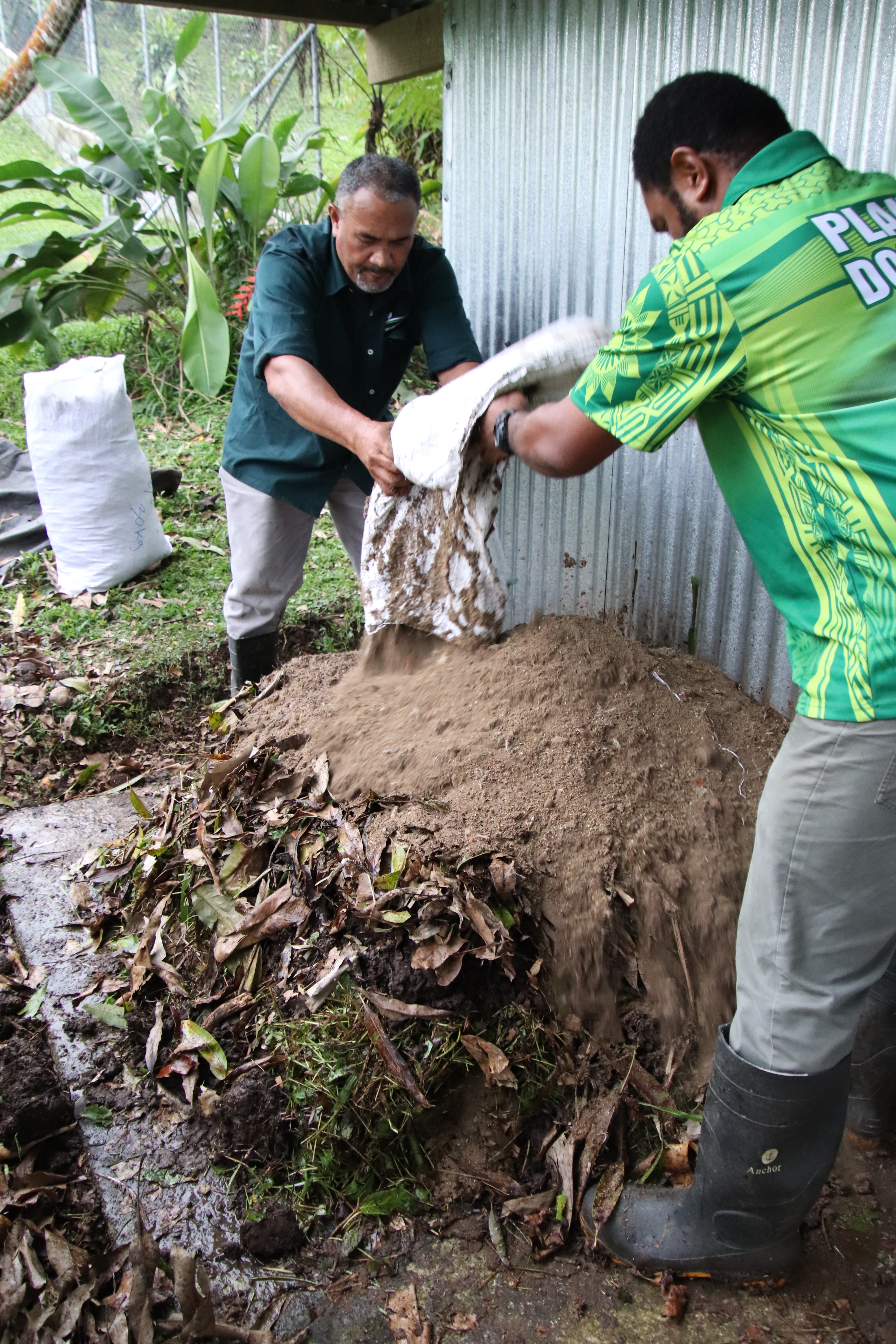 Two men adding soil from a bag to a garden bed