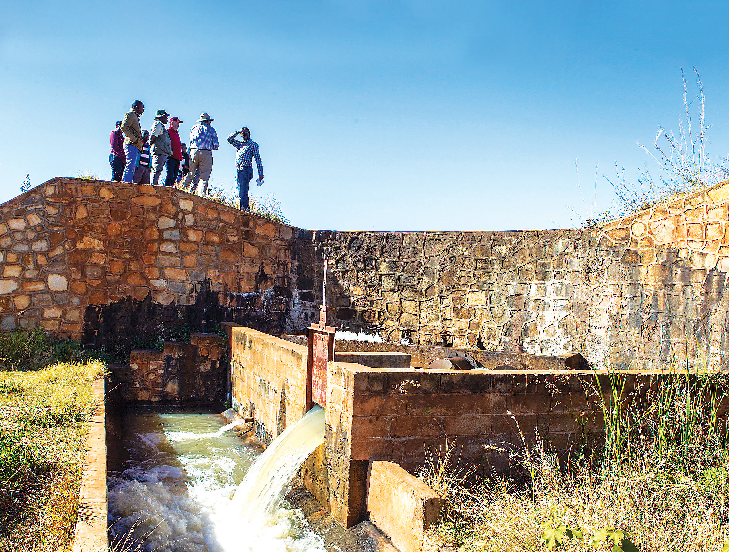 a group of people standing on to top of a rock wall as part of a water irrigation system