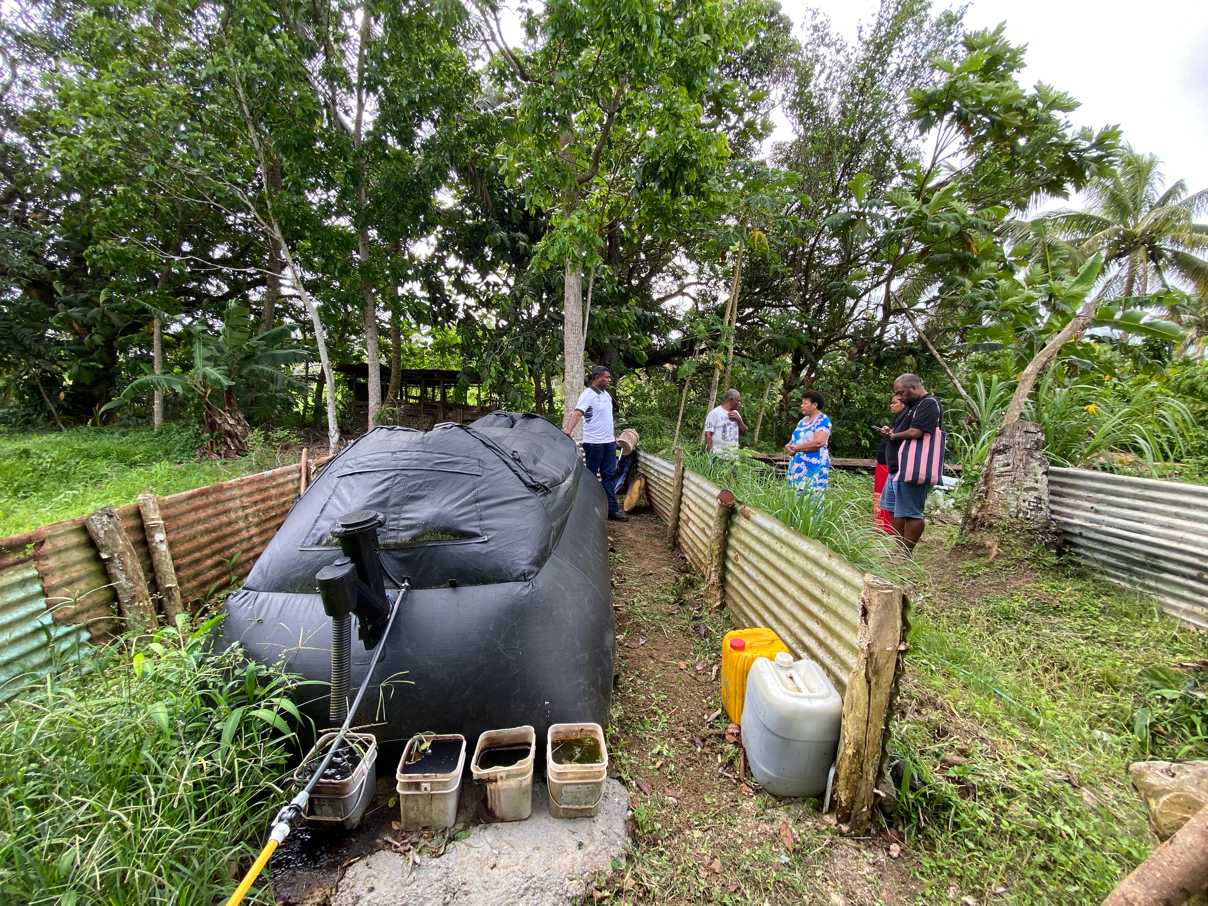 outdoors, trees, a small area fences a large black, airtight, high-density polyethylene container.