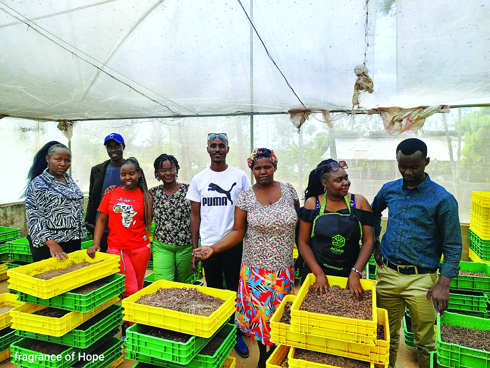 a group of people standing behind yellow and green bins filled with insect larvae