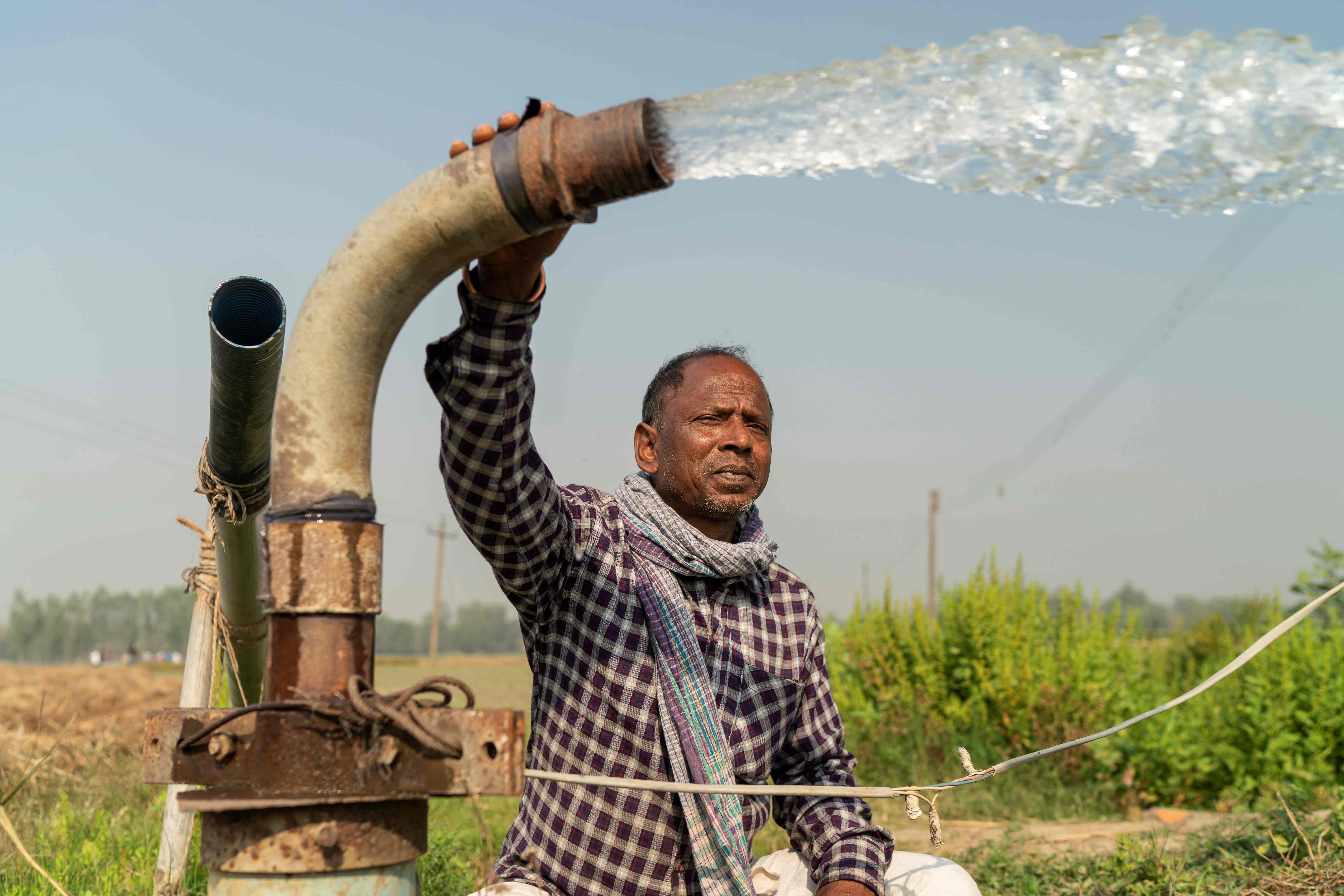 Man holding a water pump that is spraying water onto crops