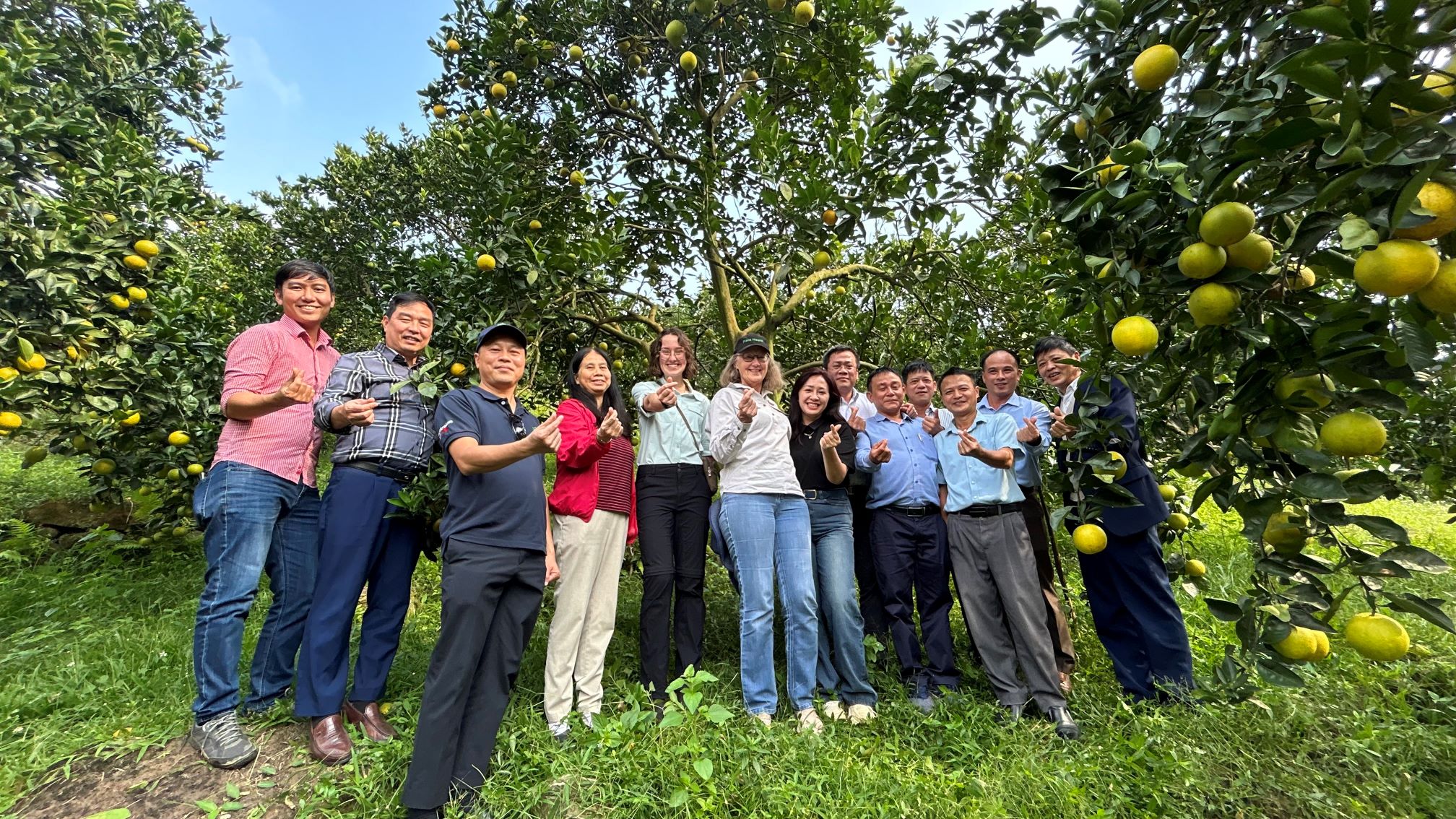 Group of people in orchard smiling with fingers in shape of love heart