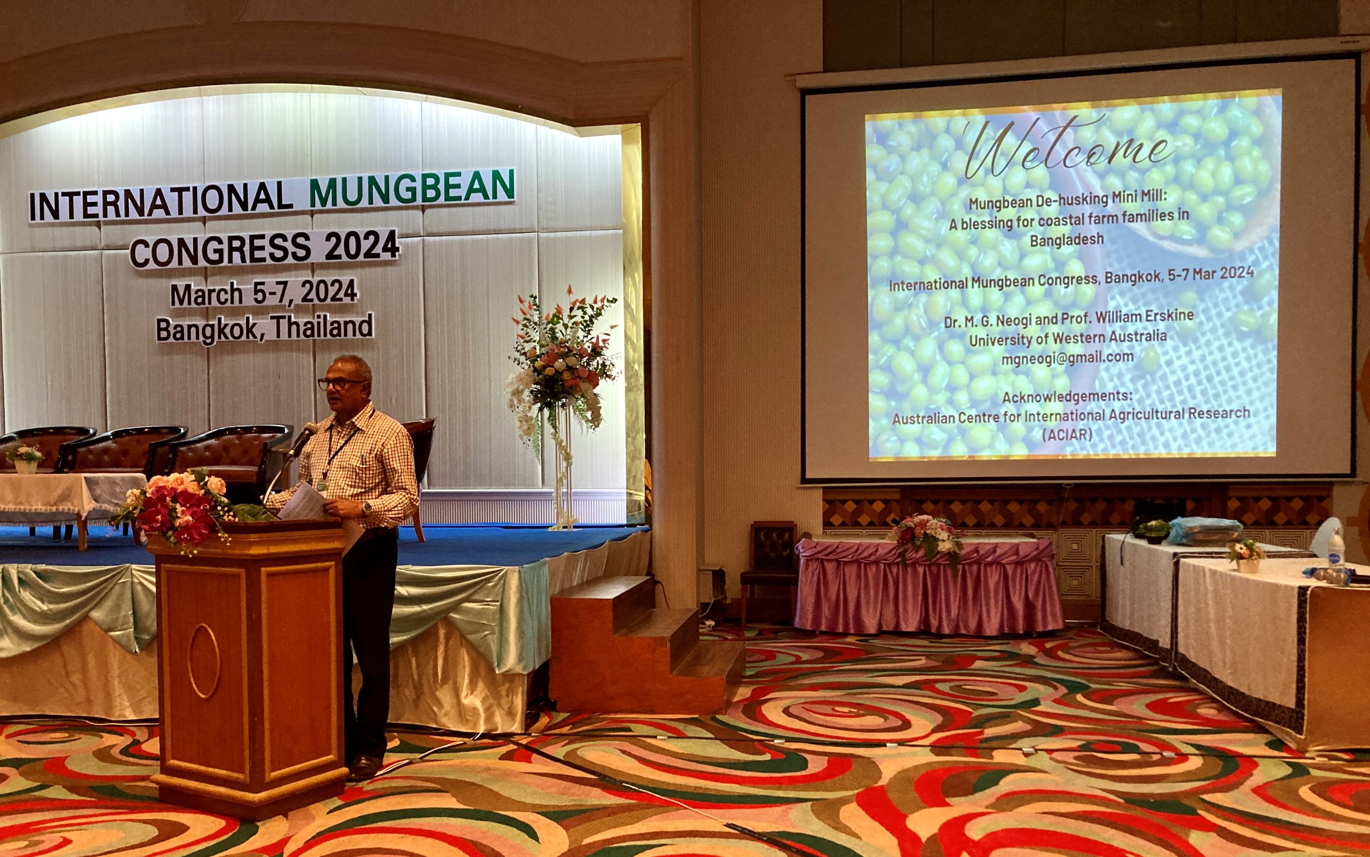 Man presenting at a podium with a large screen behind