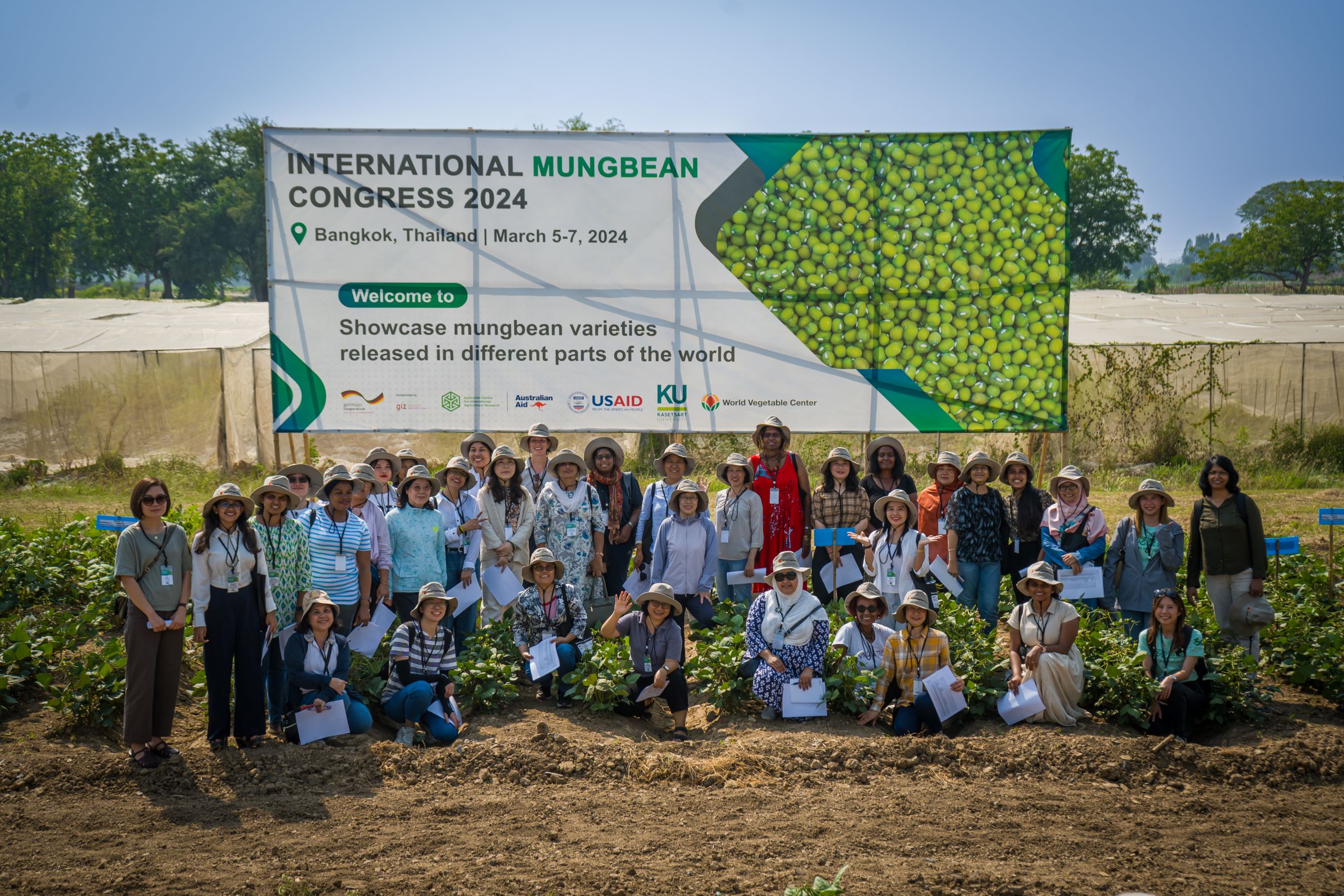 A large group of people, most wearing hats, outdoors, in front of a large sign