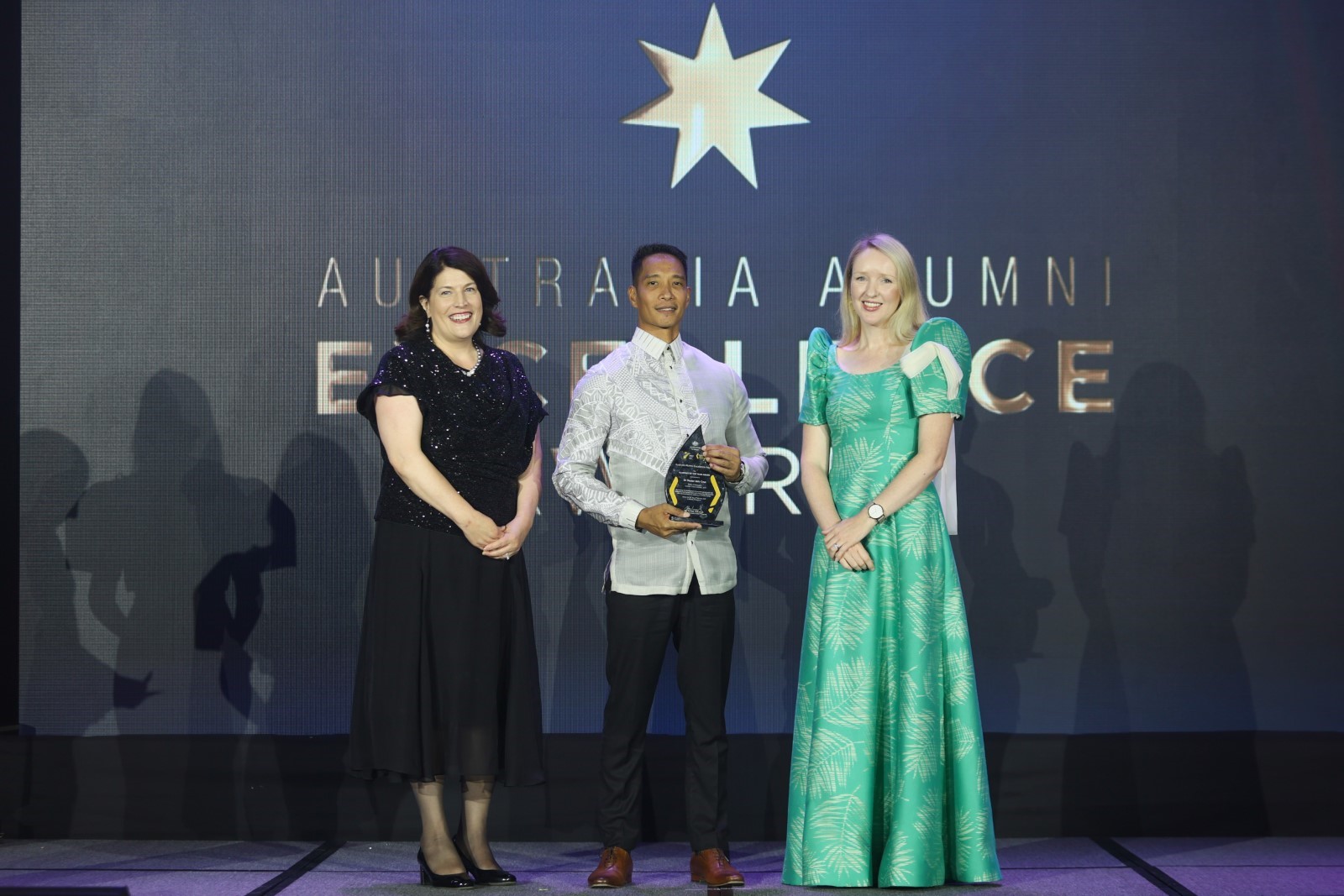 Man on stage holding an award with two presenters