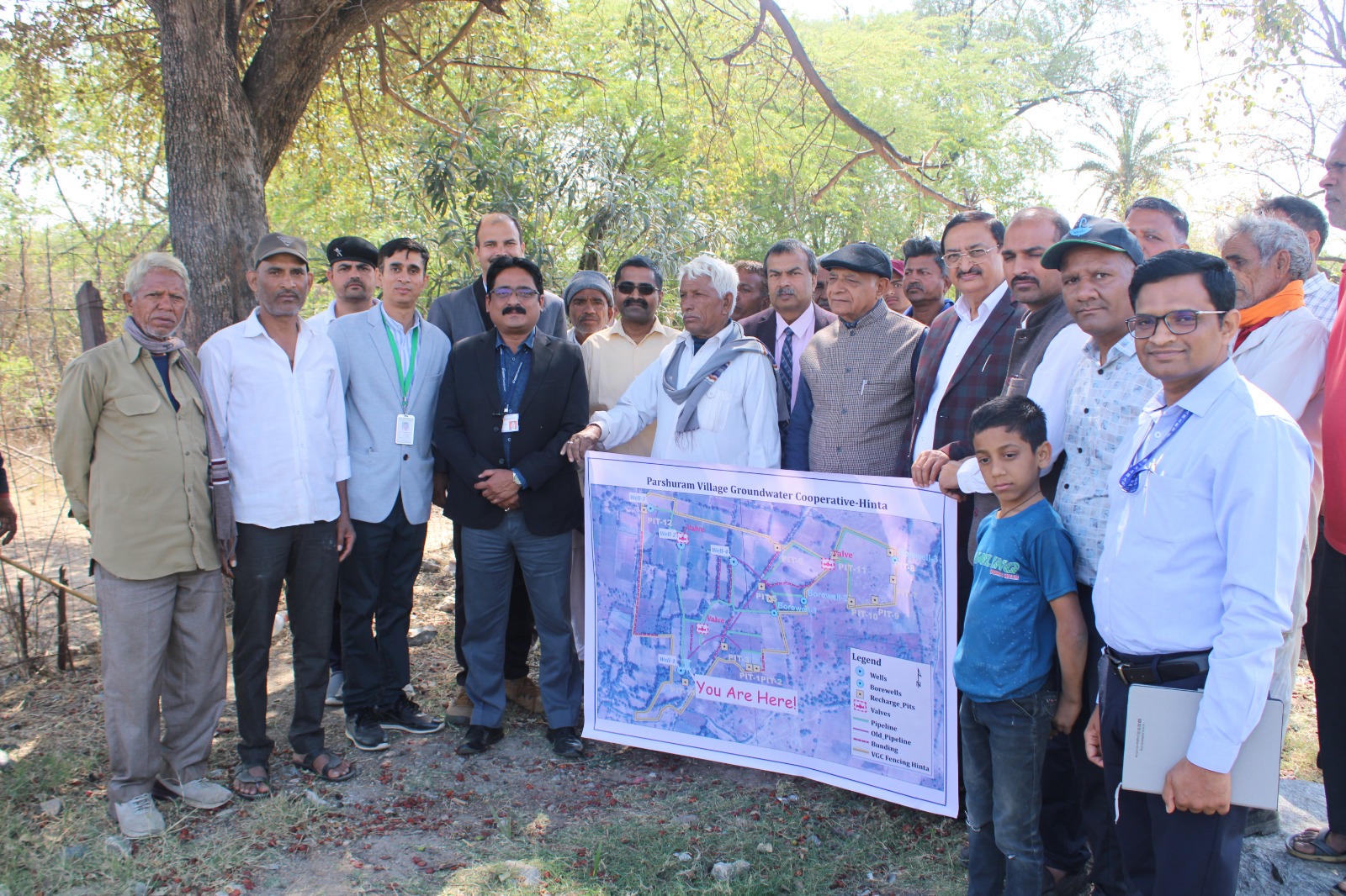 Group of individuals posing with a large map titled "Feeder Main Water Map of Corporation Garden No. 1 to 4," outdoors in a natural setting.