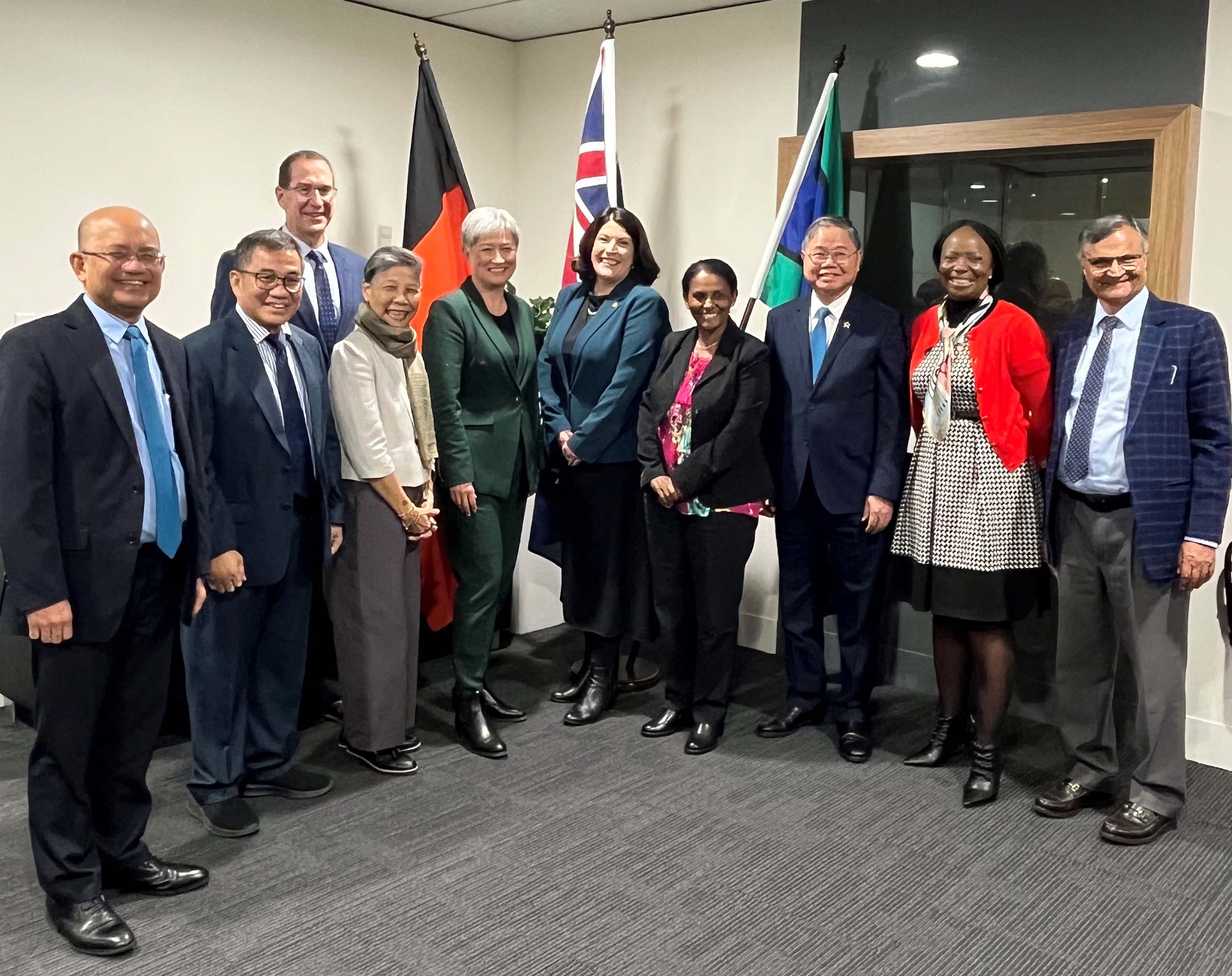 Group of nine professionals standing together in an office setting, with the Aboriginal flag, Australian flag and South Australian flag visible in the background.