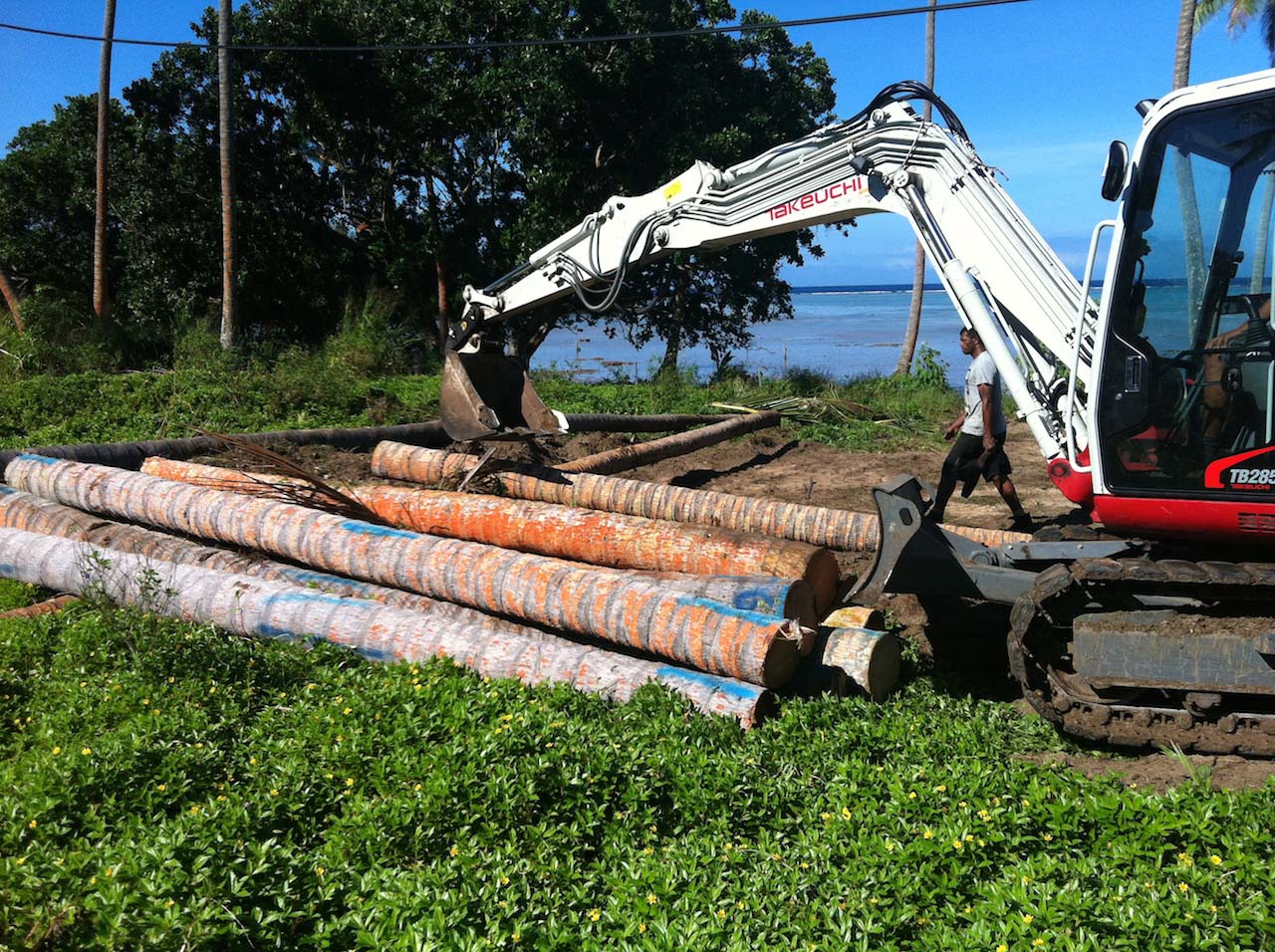 White excavator with coconut tree logs in a pile on the ground