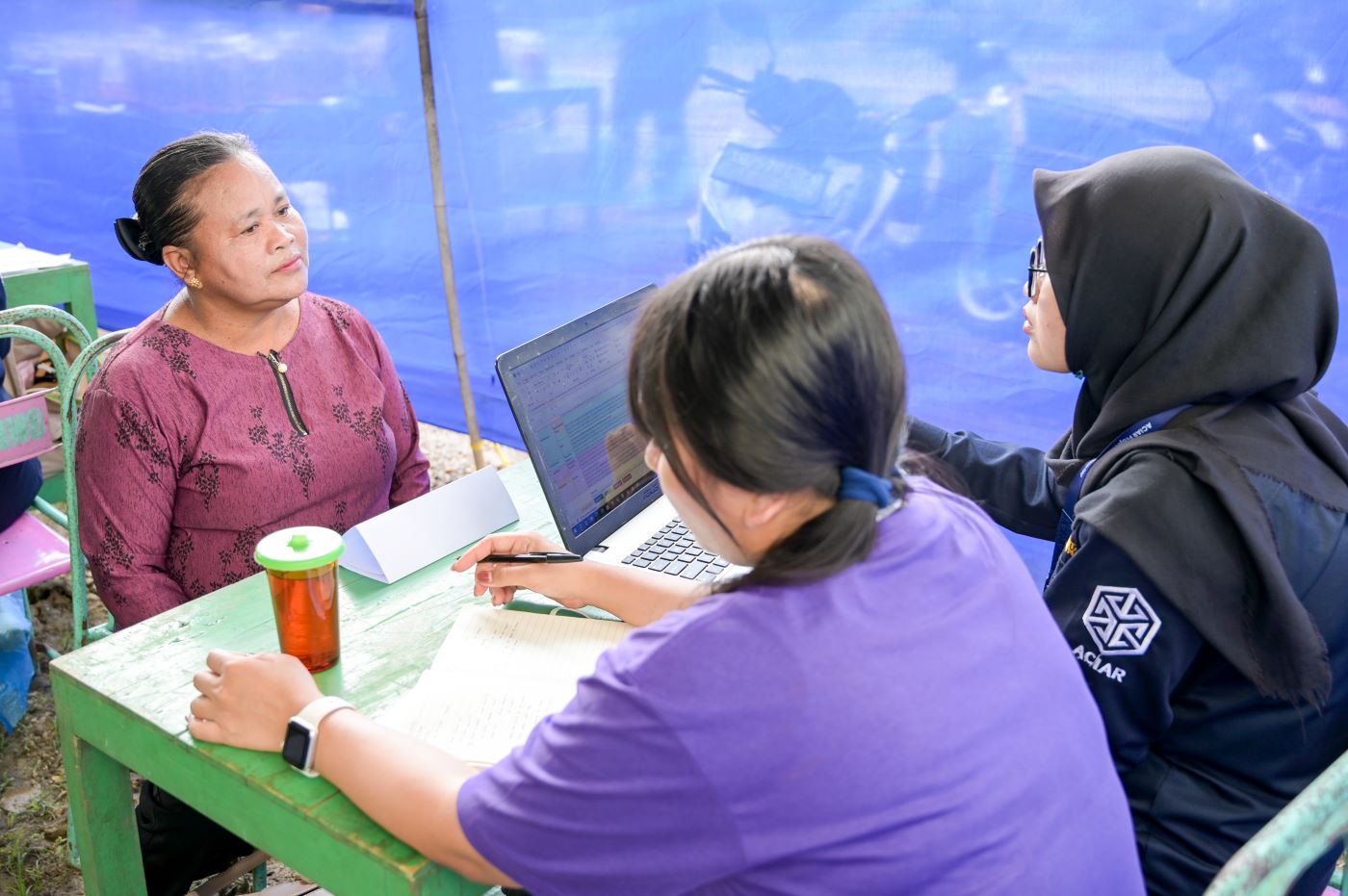 3 women sitting at a small table with a laptop computer