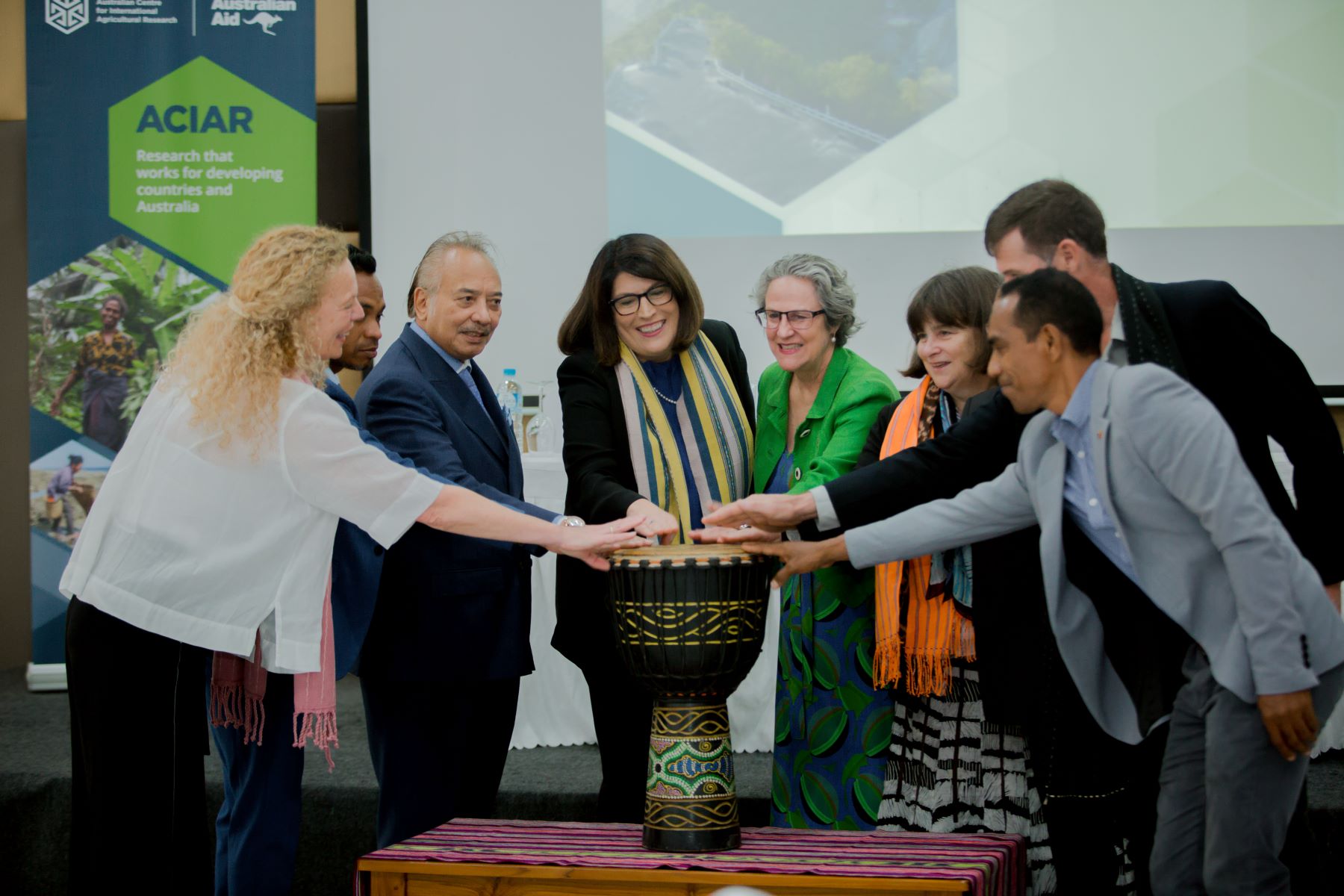 A group of people with their arms outstretched towards a drum. 