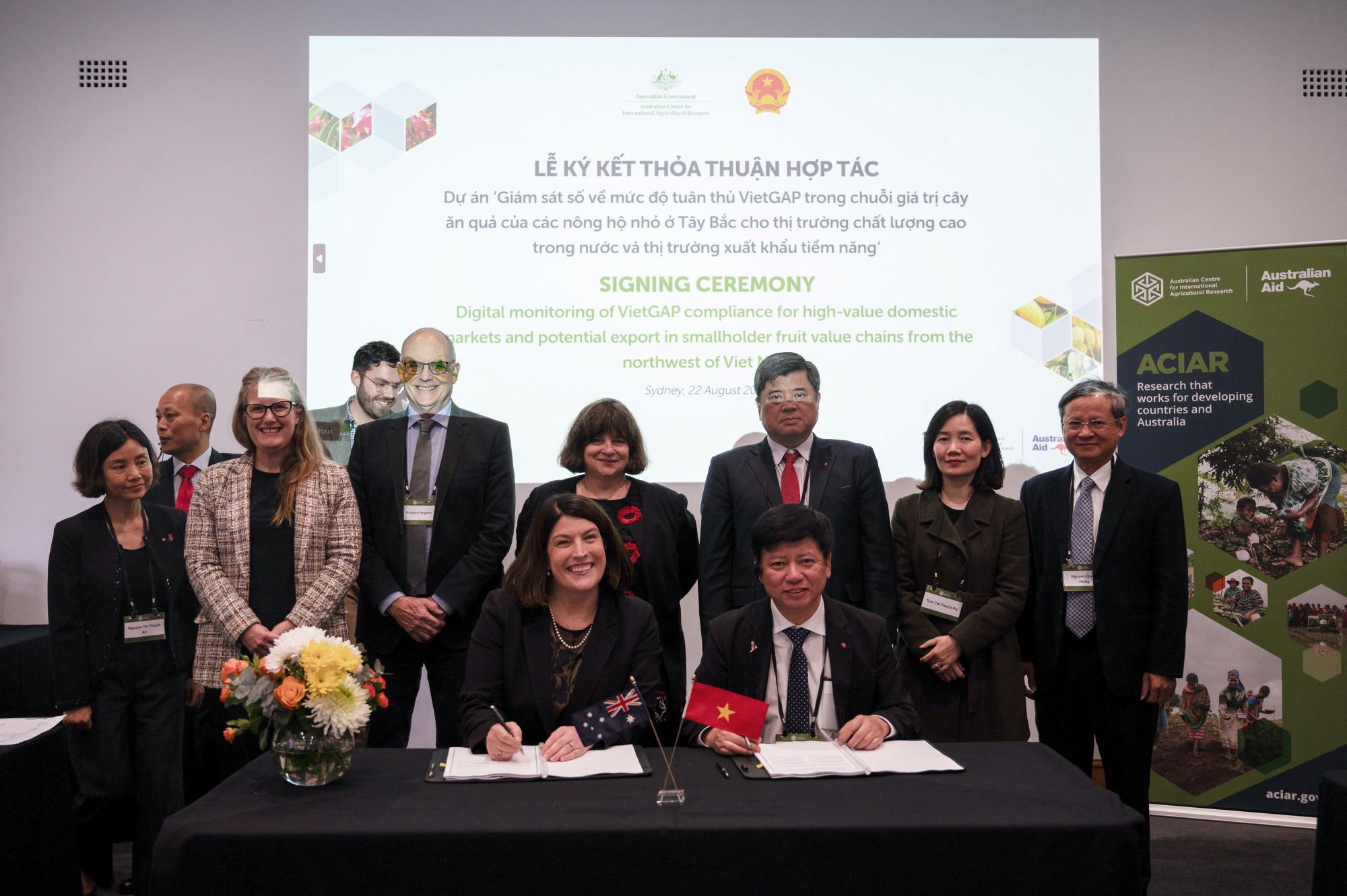 A group of people signing documents at a table and smiling at the camera