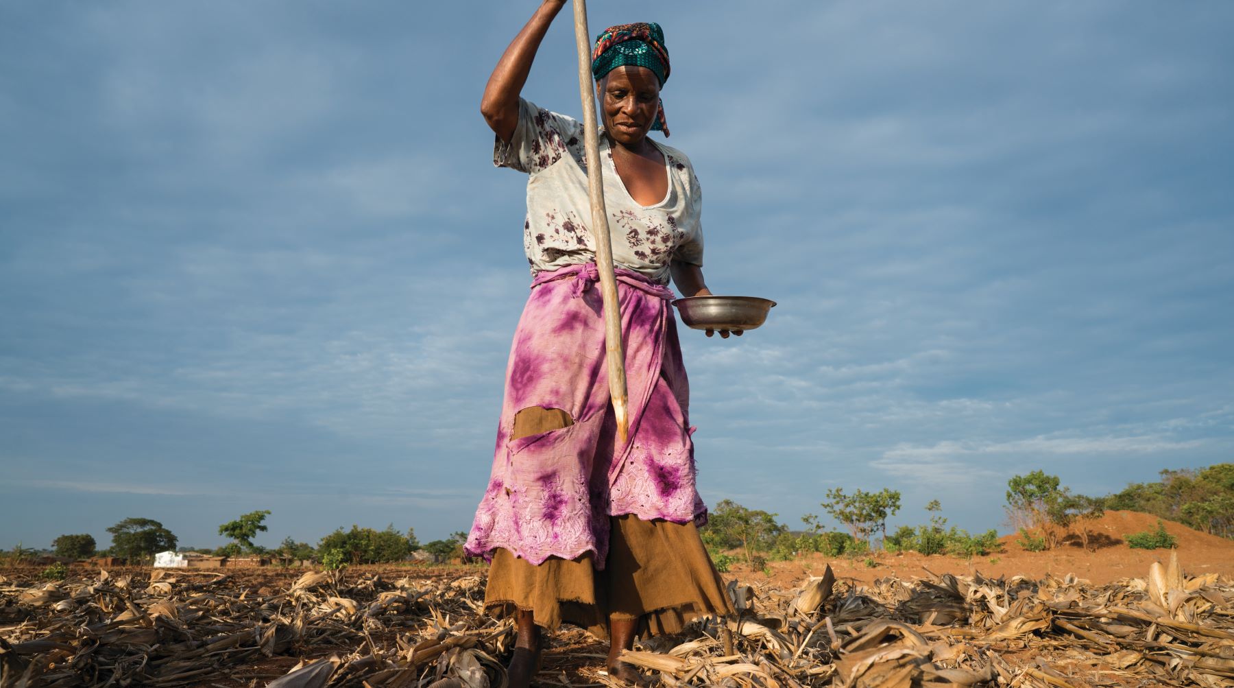 A woman holding a pan and wooden stake in a field