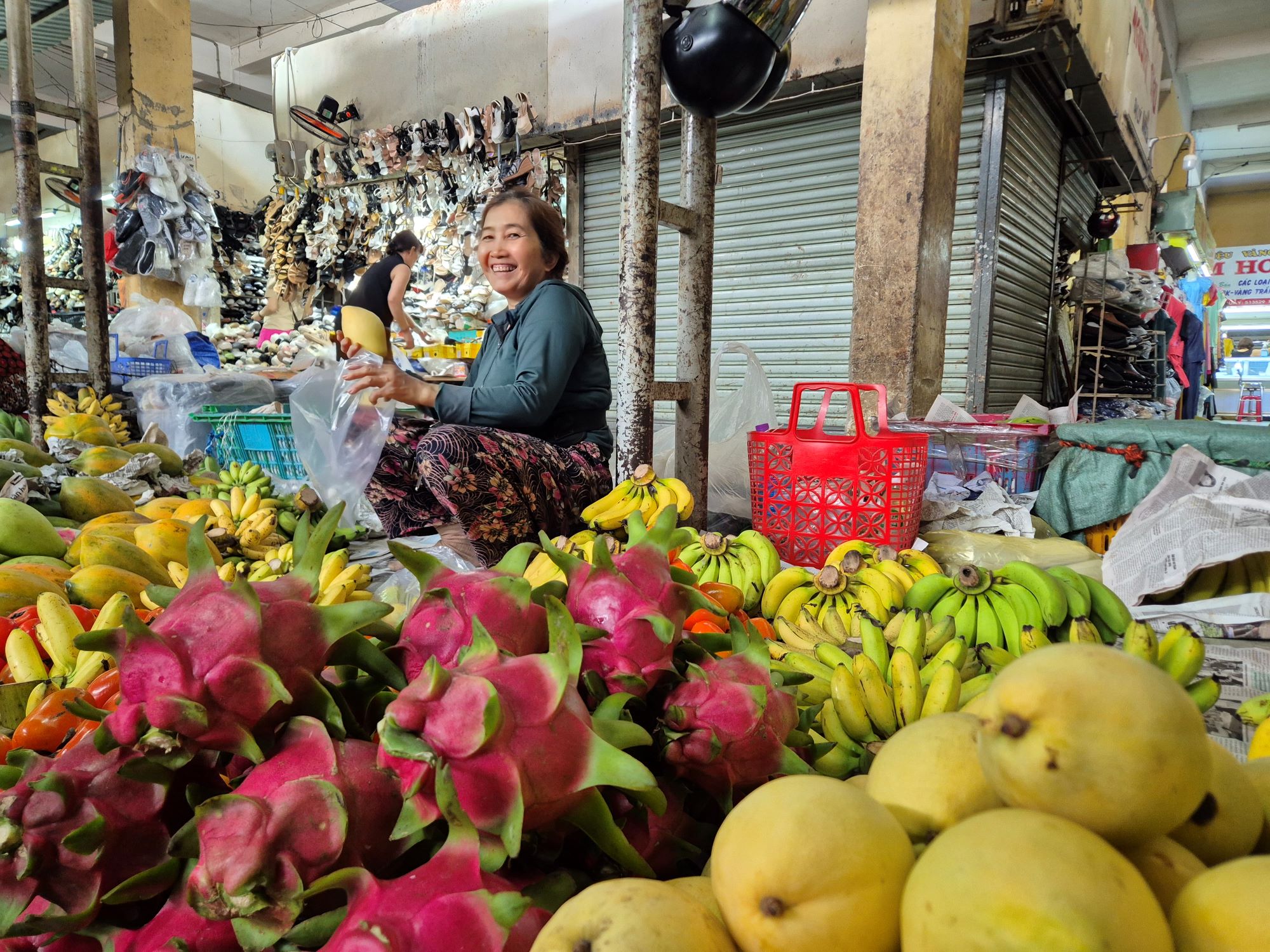 A woman sitting behind a table of dragonfruit and mangoes at a market stall