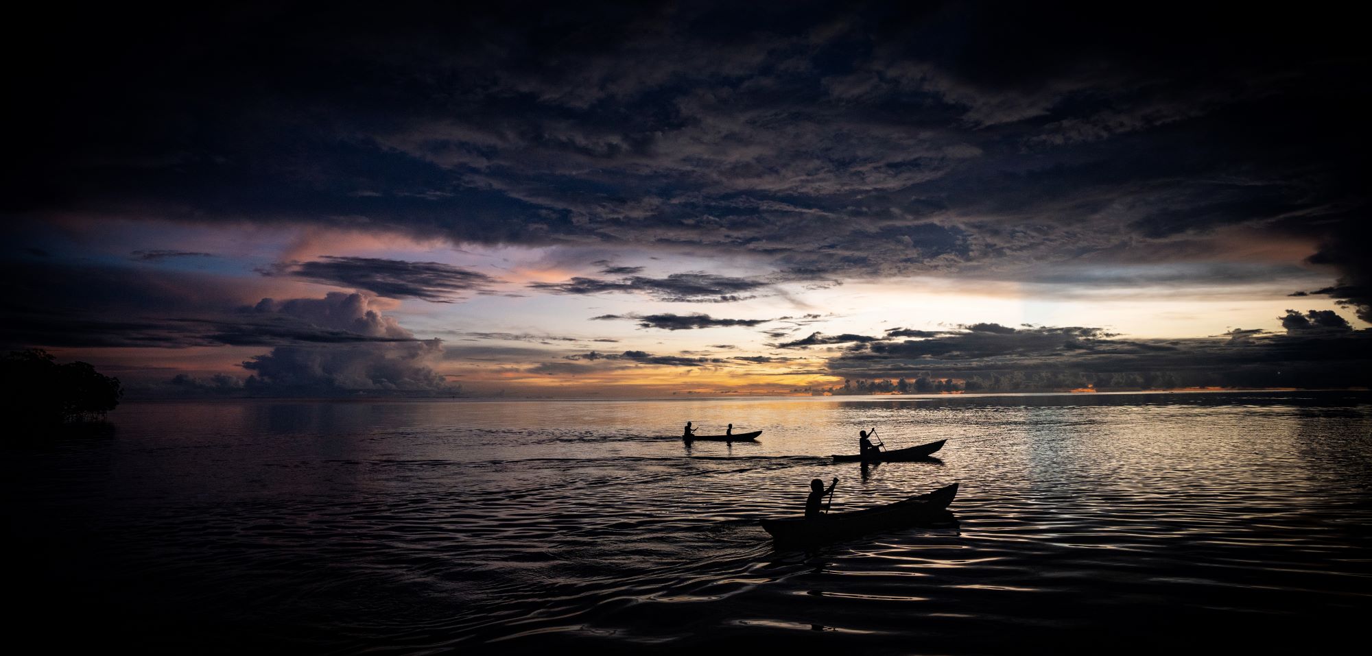 A group of people in canoes on the water at sunset
