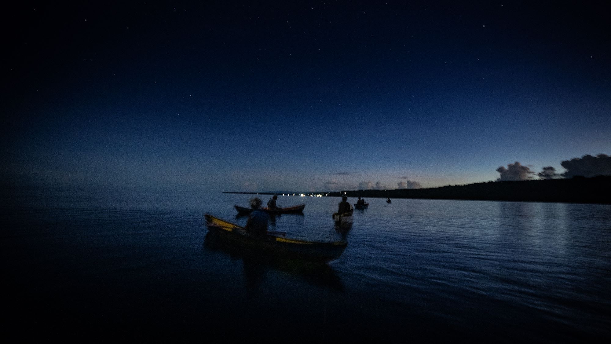 A row of canoes sitting on the water under a dark sky.
