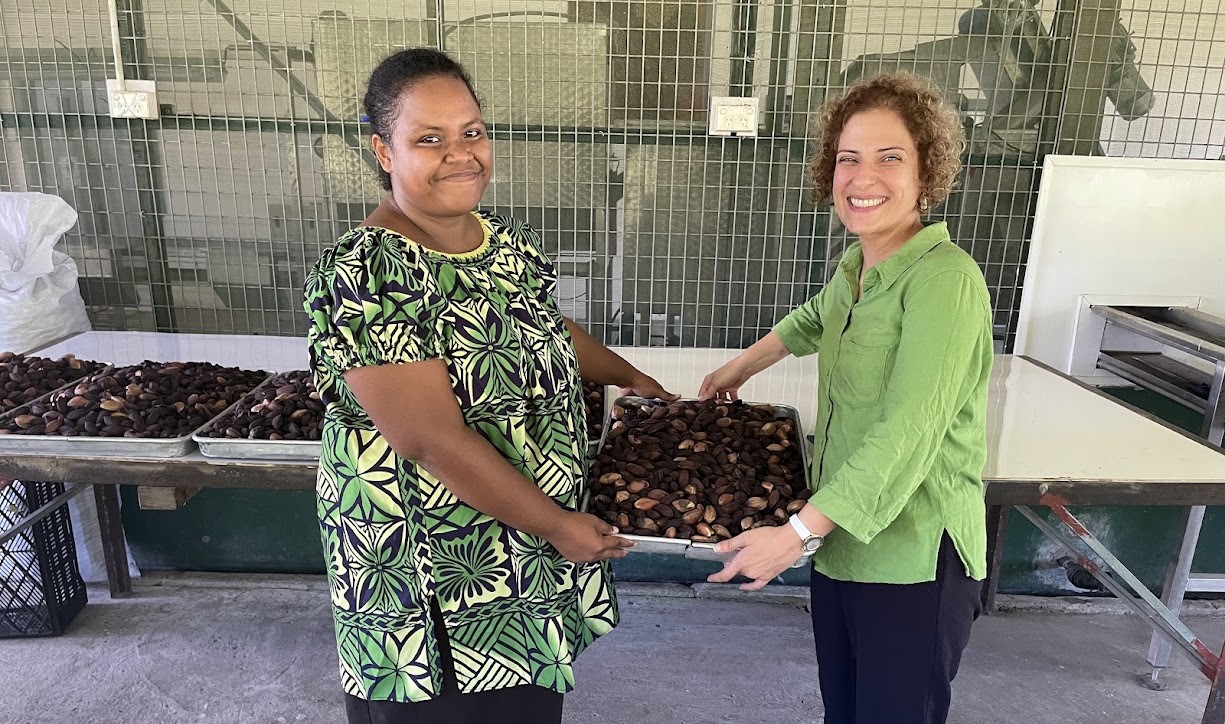 Two women in green-coloured clothing holding a tray of nuts