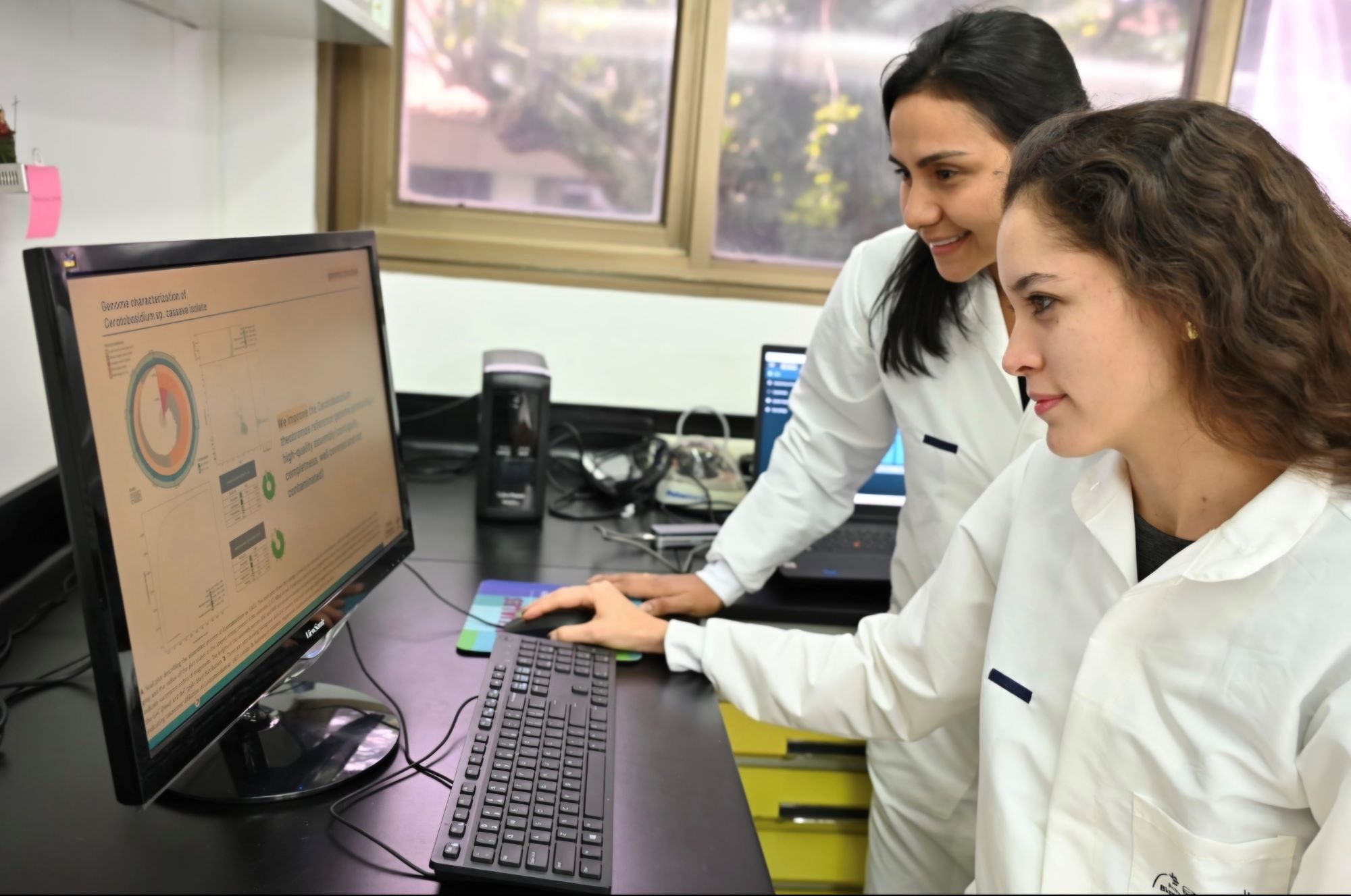 Two women in white lab coats working at a computer