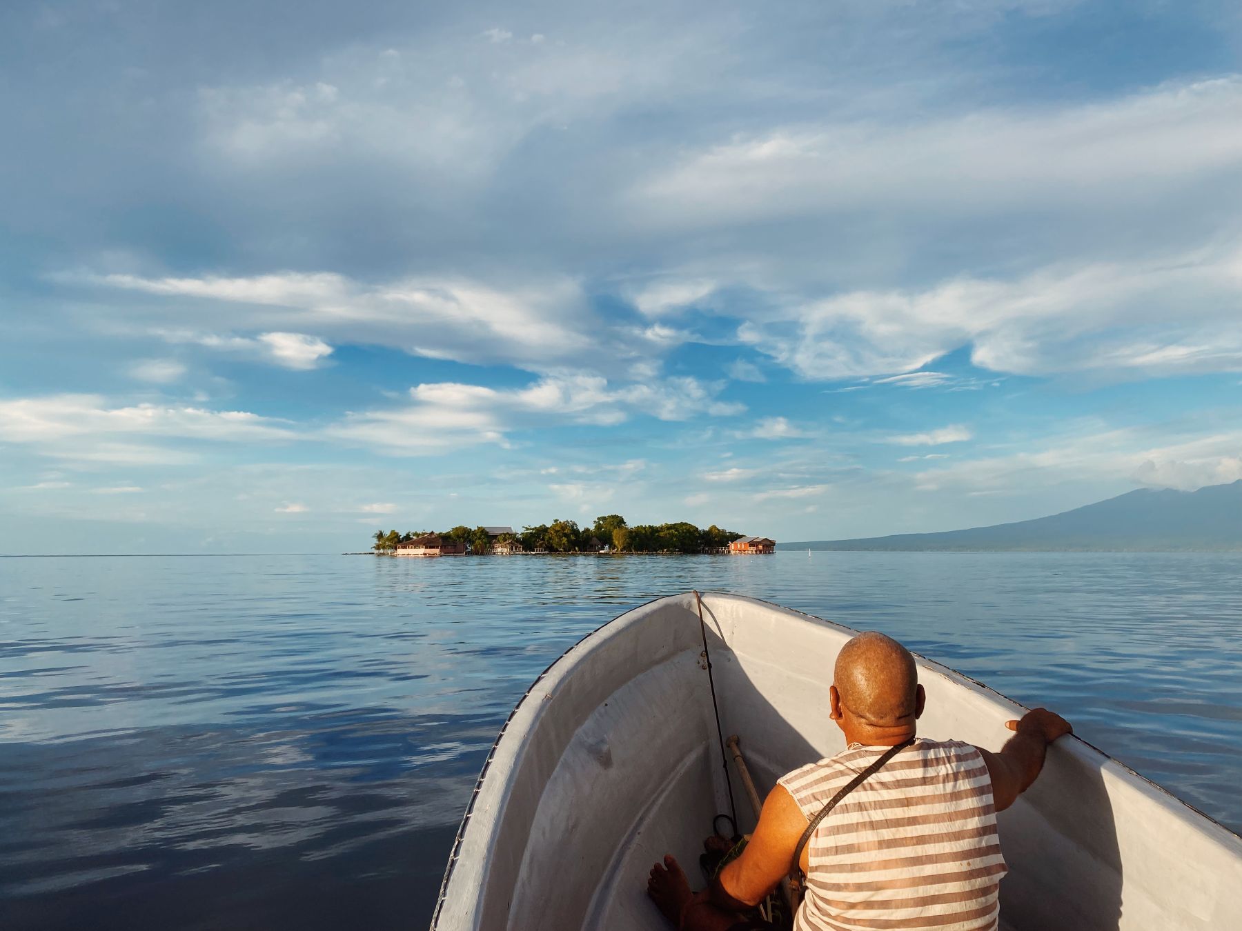 A person sitting in a boat on calm waters with an island in the distance.